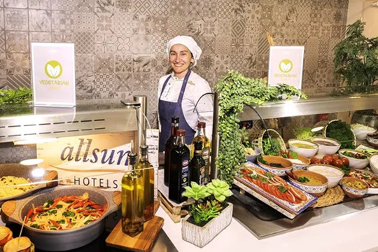 Frau mit Kochmütze und Kochschürze steht hinter einem Buffet